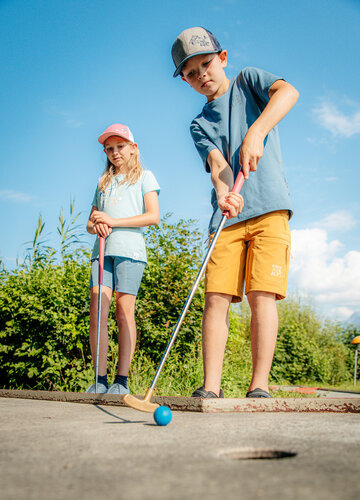 Das Bild zeigt einen Jungen und ein Mädchen beim Minigolf spielen
