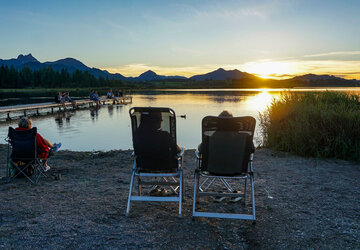 Ein Pärchen genießt den Sonnenuntergang auf Campingstühlen am Hopfensee im Allgäu