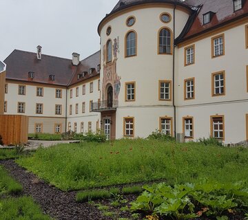 Kloster Ettal Auf dem Bild ist das Kloster Ettal zu sehen. Im Vordergrund erkennt man einen schön angelegten Kräutergarten mit grünen Planzen.