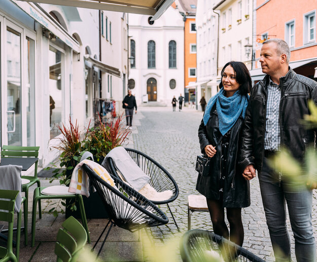Ein Paar spaziert Hand in Hand durch eine malerische Kopfsteinpflasterstraße in der Füssener Altstadt, umgeben von Geschäften und Cafés.