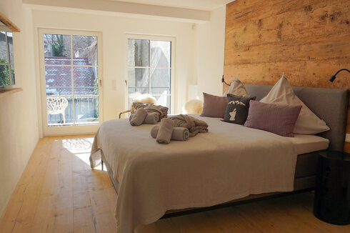 Ein gemütliches Schlafzimmer mit Blick durch die Flügeltüren. Die Wände sind mit Holzpaneelen verkleidet, die Einrichtung ist schlicht und modern. 