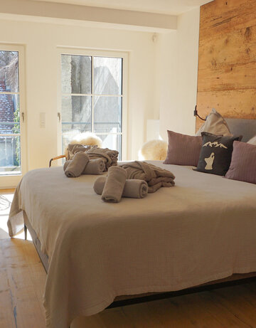 Ein gemütliches Schlafzimmer mit Blick durch die Flügeltüren. Die Wände sind mit Holzpaneelen verkleidet, die Einrichtung ist schlicht und modern. 