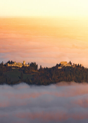 Eine Burgruine schmiegt sich in den Nebel, ein Ort voller Geschichten und Geheimnisse. Ein atemberaubender Sonnenuntergang verstärkt die mystische Stimmung.