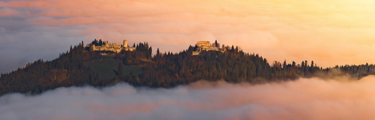 Eine Burgruine schmiegt sich in den Nebel, ein Ort voller Geschichten und Geheimnisse. Ein atemberaubender Sonnenuntergang verstärkt die mystische Stimmung.