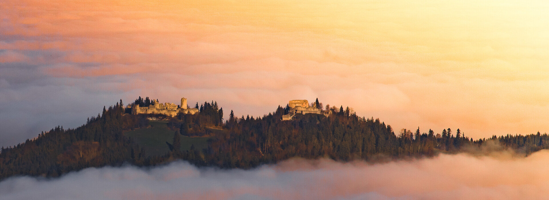 Eine Burgruine schmiegt sich in den Nebel, ein Ort voller Geschichten und Geheimnisse. Ein atemberaubender Sonnenuntergang verstärkt die mystische Stimmung.