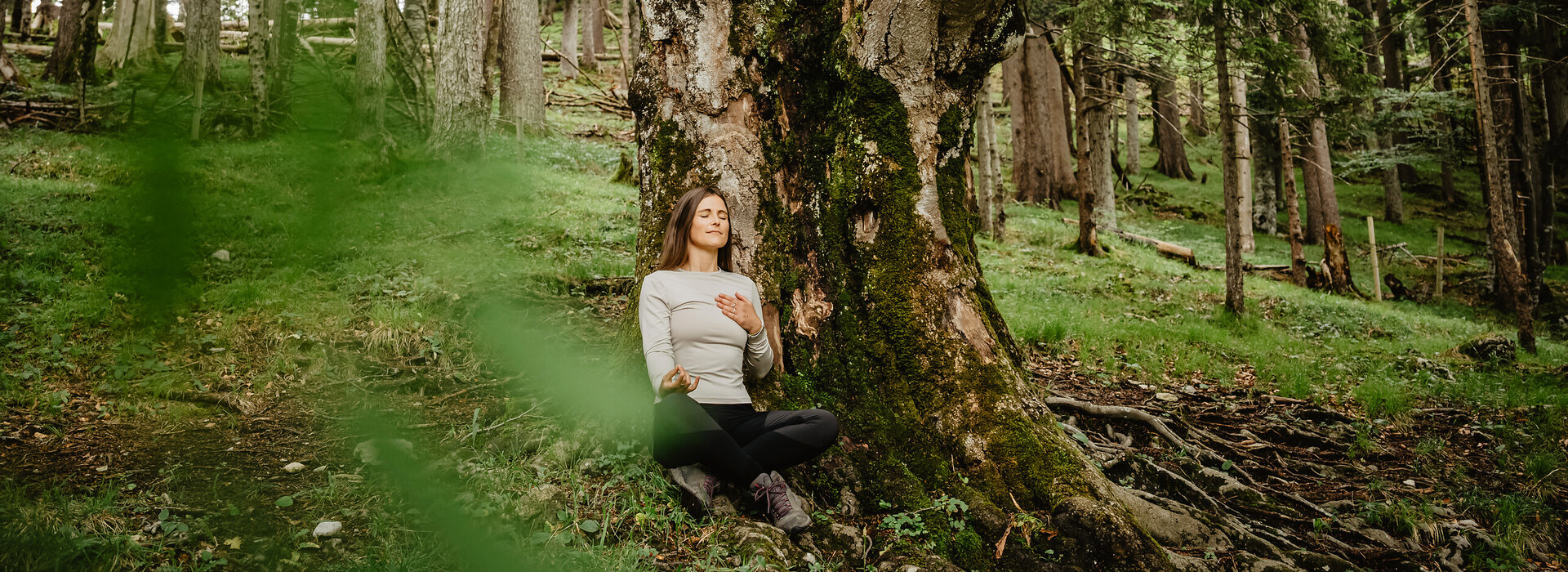 Das Bild zeigt eine Frau, die an einem Baum lehnt und meditiert