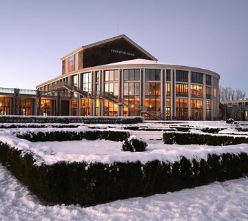 Auf dem Bild ist der verschneite Barockgarten sowie der runde Kubus des Festspielhaus Neuschwanstein zu sehen