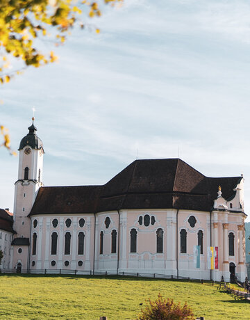 Eine historisch weiße Kirche mit roten Dächern in einer grünen Landschaft.