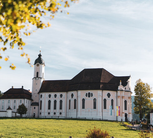 Eine historisch weiße Kirche mit roten Dächern in einer grünen Landschaft.