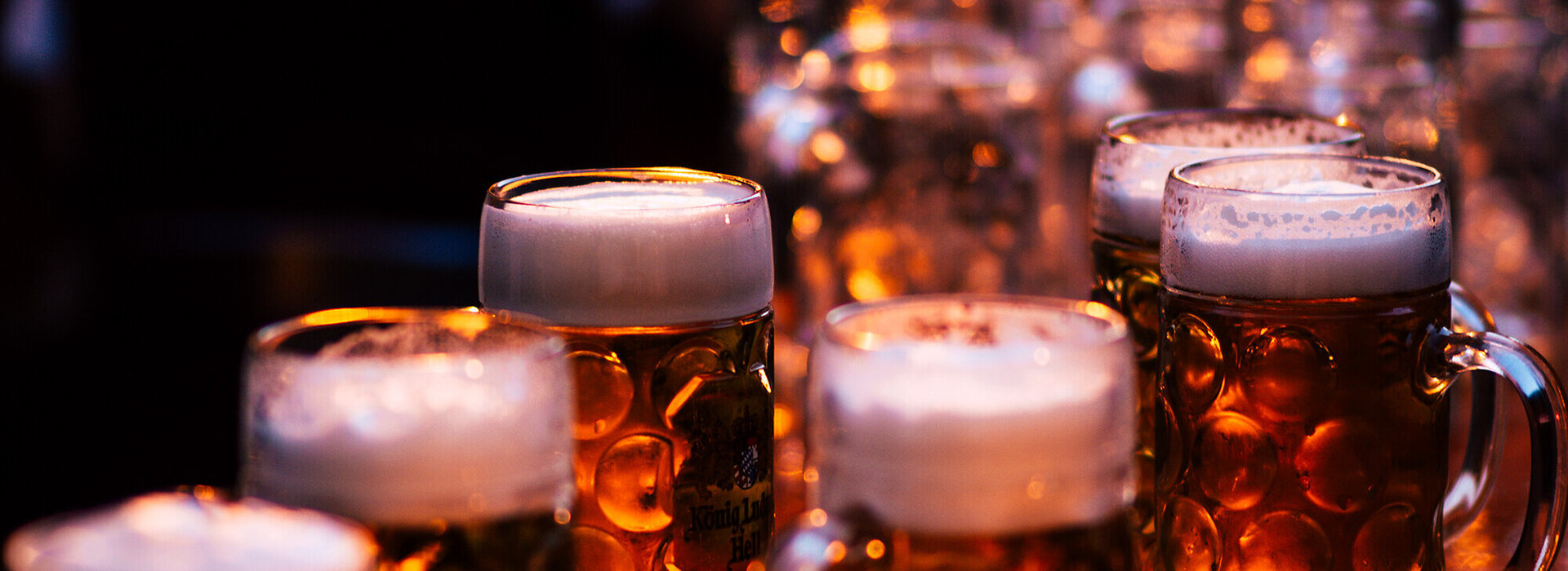 Man sieht eine Platte mit mehreren Bierkrügen, die mit Schaum bedeckt sind. Die Beleuchtung ist gedämpft und warm, was eine gemütliche und entspannte Atmosphäre schafft.
