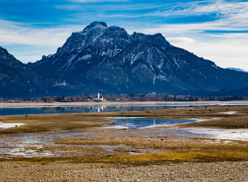Blick über den teilabgelassenen Forggensee auf Schloss Neuschwanstein und den Säuling.