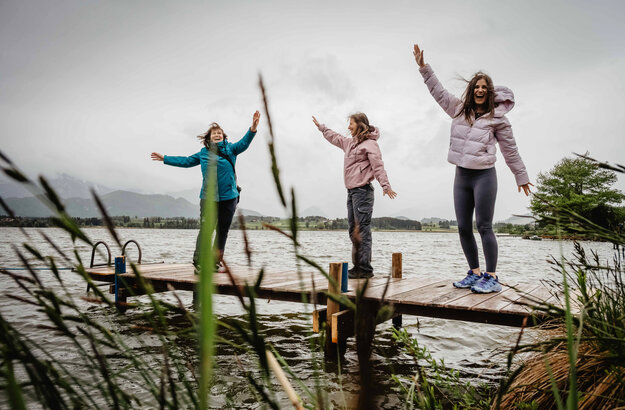 Drei Frauen springen auf einem Steg am Hopfensee in die Luft