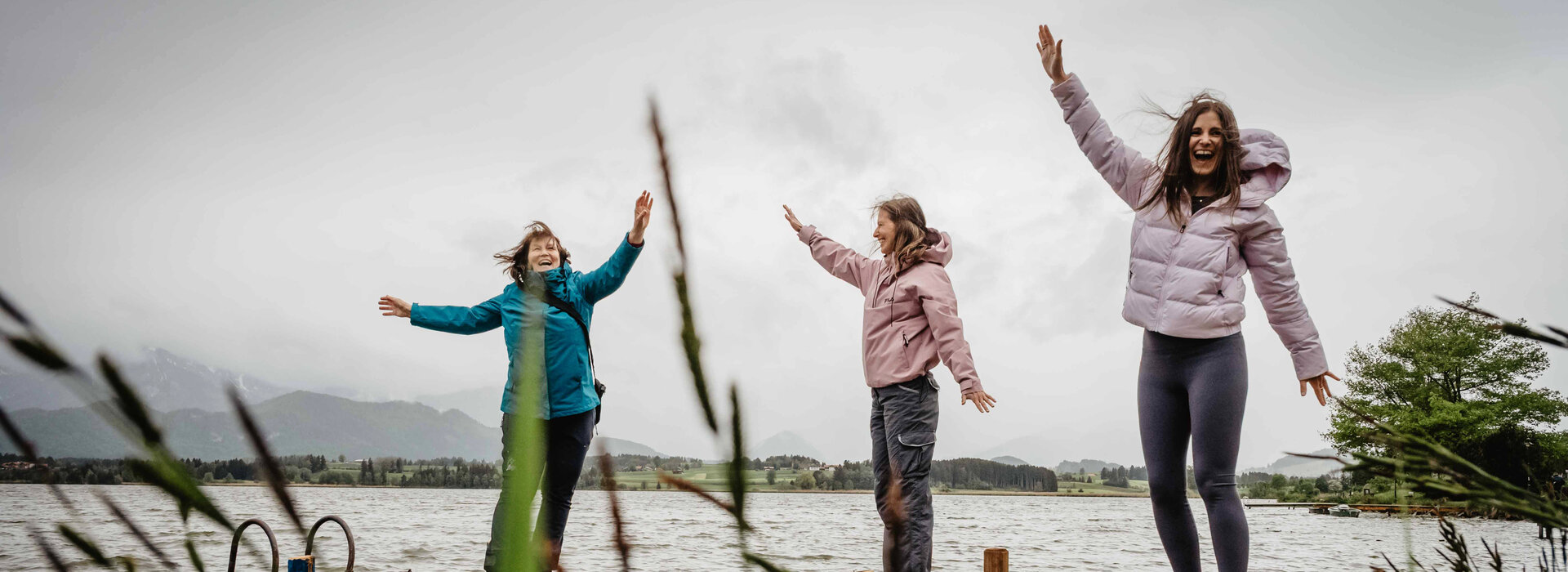 Drei Frauen machen auf einem Steg am See Armübungen