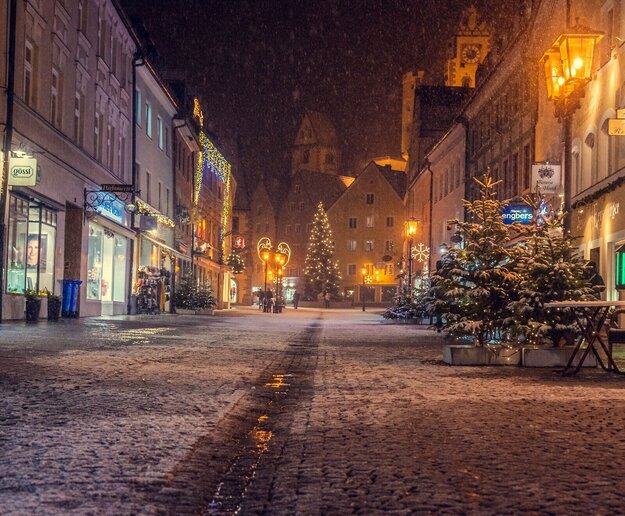  Das Bild fängt eine friedliche Nachtszene in einer europäischen Stadt ein. Die Straße, die mit Gebäuden gesäumt ist, wird vom sanften Glanz der Straßenlaternen erfüllt. Der Kopfsteinpflasterweg, auf dem es vor kurzem geregnet hat, reflektiert das Licht, was eine magische Note zur Szene hinzufügt.