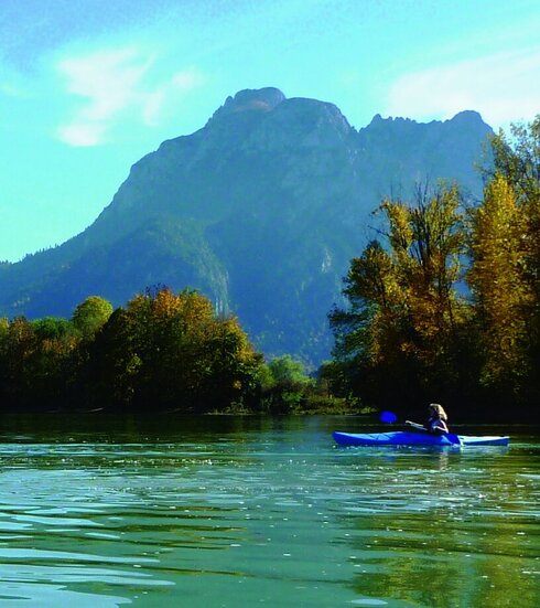 Das Bild zeigt ein langes Drachenboot auf dem Forggensee. Im Hintergrund sind die schönen Alpen zu erkennen.