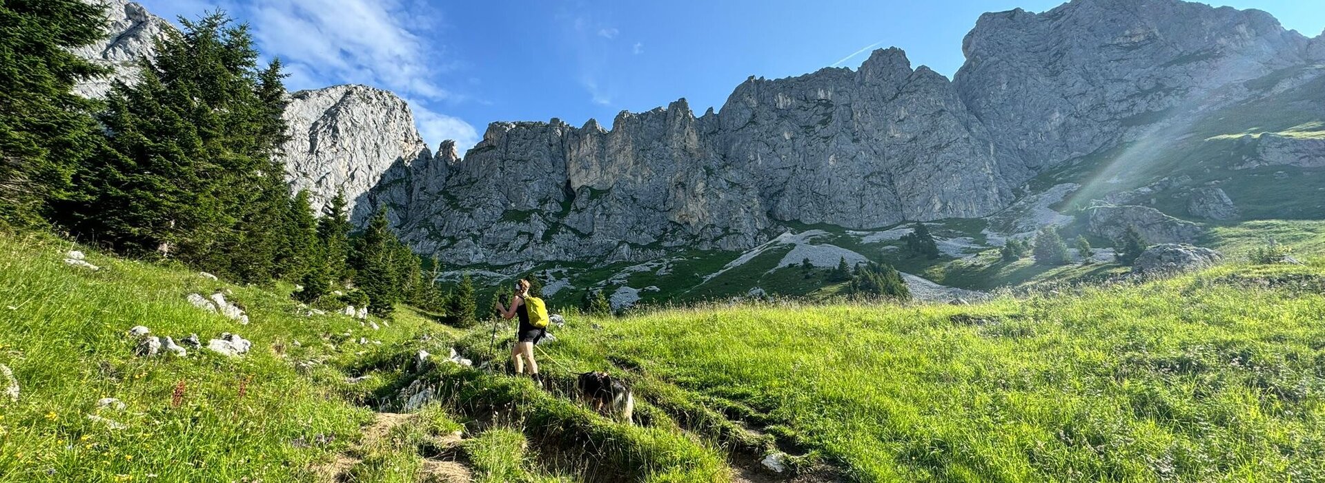 Das Bild zeigt eine wandernde Frau mit einem Hund in den Bergen.
