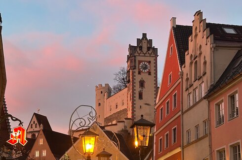 Sonnenuntergang in der Reichenstraße in der Füssener Altstadt. Die bunten Häsuer und das Hohe Schloss glänzen rot in der untergehenden Sonne. 