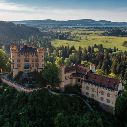 Das prächtige Schloss Hohenschwangau thront auf einem Hügel inmitten einer grünen Landschaft. Die Aussicht bietet eine idyllische Kulisse.