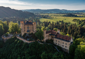 Das prächtige Schloss Hohenschwangau thront auf einem Hügel inmitten einer grünen Landschaft. Die Aussicht bietet eine idyllische Kulisse.