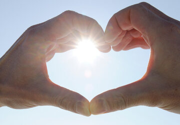 Das Bild zeigt zwei Hände, die ein Herz formen. Durch die Hände strahlt die Wintersonne vor dem blauen, klaren Himmel.