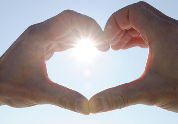 Das Bild zeigt zwei Hände, die ein Herz formen. Durch die Hände strahlt die Wintersonne vor dem blauen, klaren Himmel.
