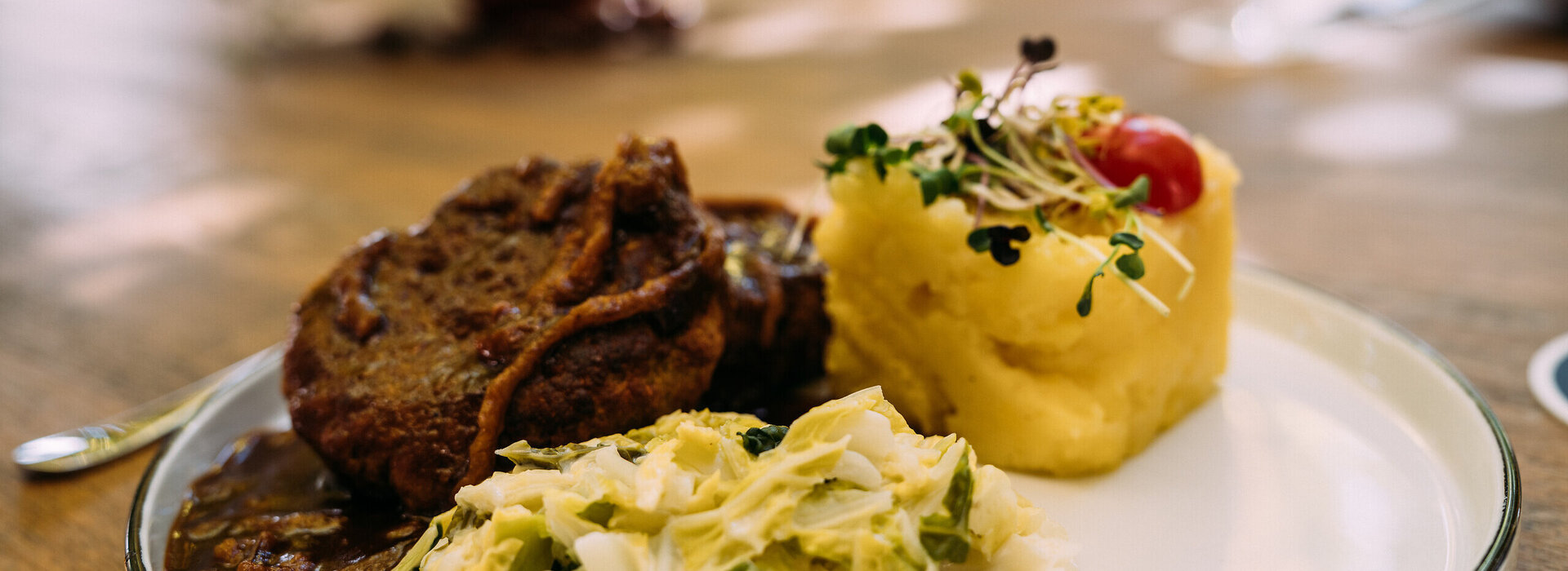 Ein deftiges Gericht mit Fleisch, Kartoffelpüree und Krautsalat wird auf einem Teller serviert.