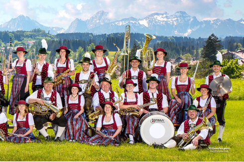 Vereinsbild einer Musikkapelle im Frühling im Ostallgäu. Die Musiker heben ihre Instrumente in die Luft und haben alle verschiedene Posen.