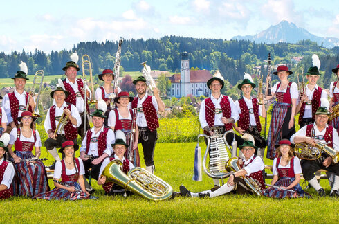 Vereinsbild einer Musikkapelle im Frühling im Ostallgäu. Die Musiker heben ihre Instrumente in die Luft und haben alle verschiedene Posen.