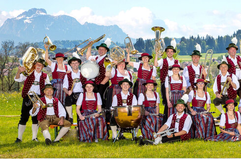 Vereinsbild einer Musikkapelle im Frühling im Ostallgäu. Die Musiker heben ihre Instrumente in die Luft und haben alle verschiedene Posen.