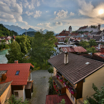 Die malerische Füssener Altstadt mit roten Dächern erstreckt sich am Ufer des Leches. Im Hintergrund rücken majestätische Berge in den Himmel.