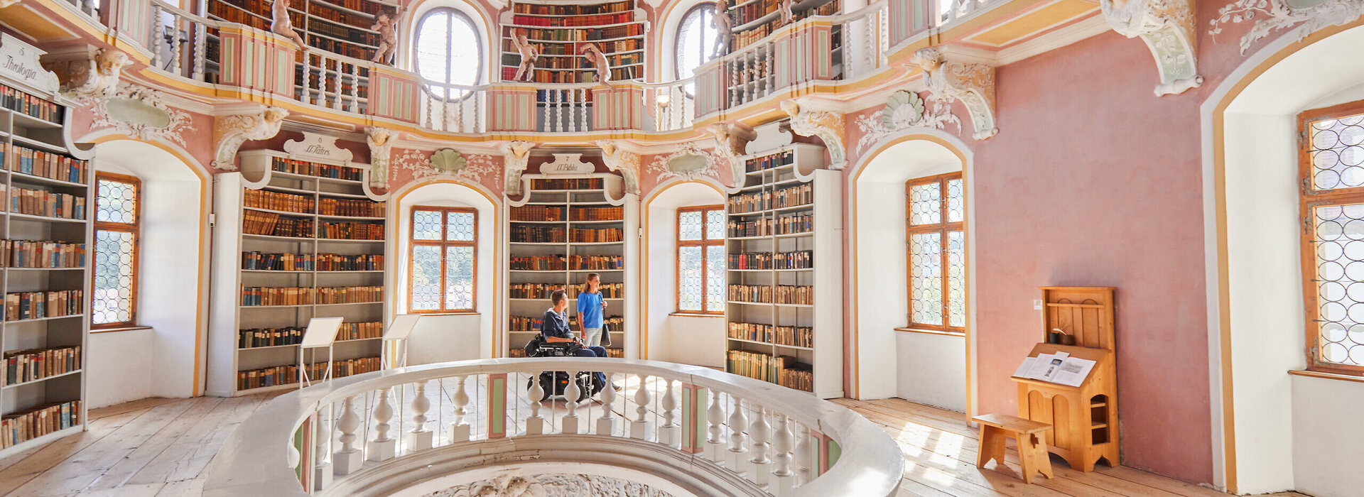 Die Bibliothek des Hohen Schlosses in Füssen mit hohen Regalen und einem beeindruckenden Rundbogen. Das Bild zeigt einen Raum voller Wissen und Geschichte.
