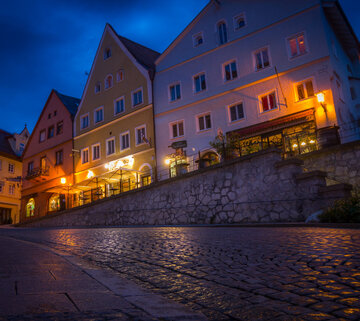 Das Bild zeigt ein Gebäude in der Füssener Altstadt mit vielen beleuchteten Fenstern. Der Boden spiegelt das Licht wider.
