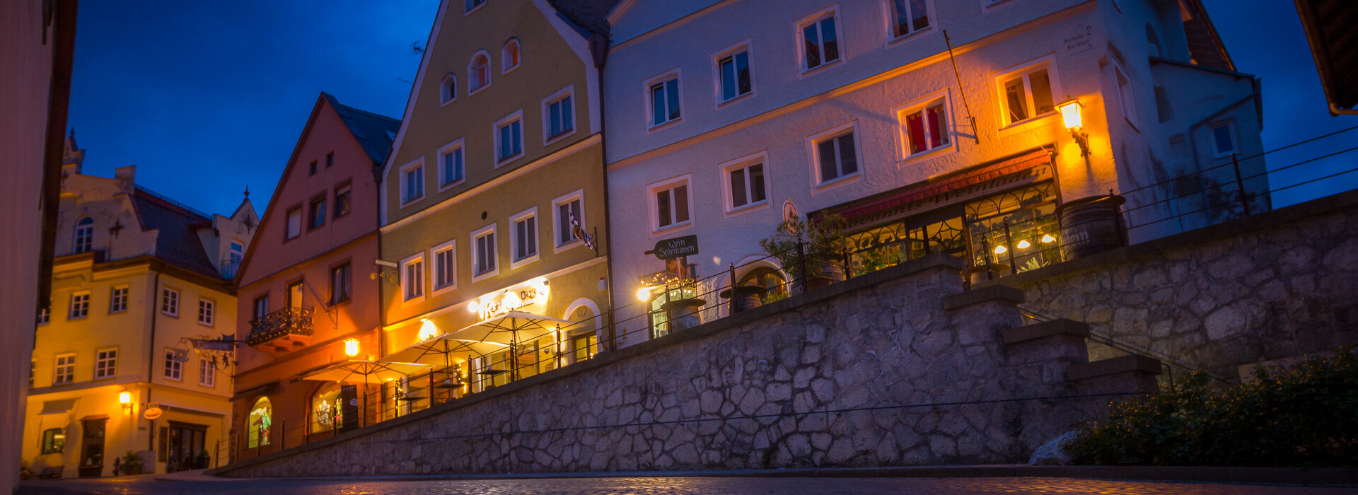 Das Bild zeigt ein Gebäude in der Füssener Altstadt mit vielen beleuchteten Fenstern. Der Boden spiegelt das Licht wider.