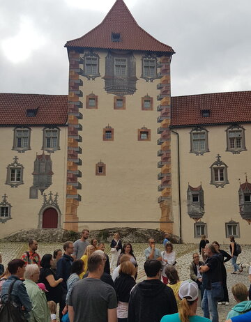 Eine Gruppe von Touristen betrachtet das prächtige Hohe Schloss in Füssen. Die Fassade mit ihren kunstvollen Erkern ist beeindruckend.