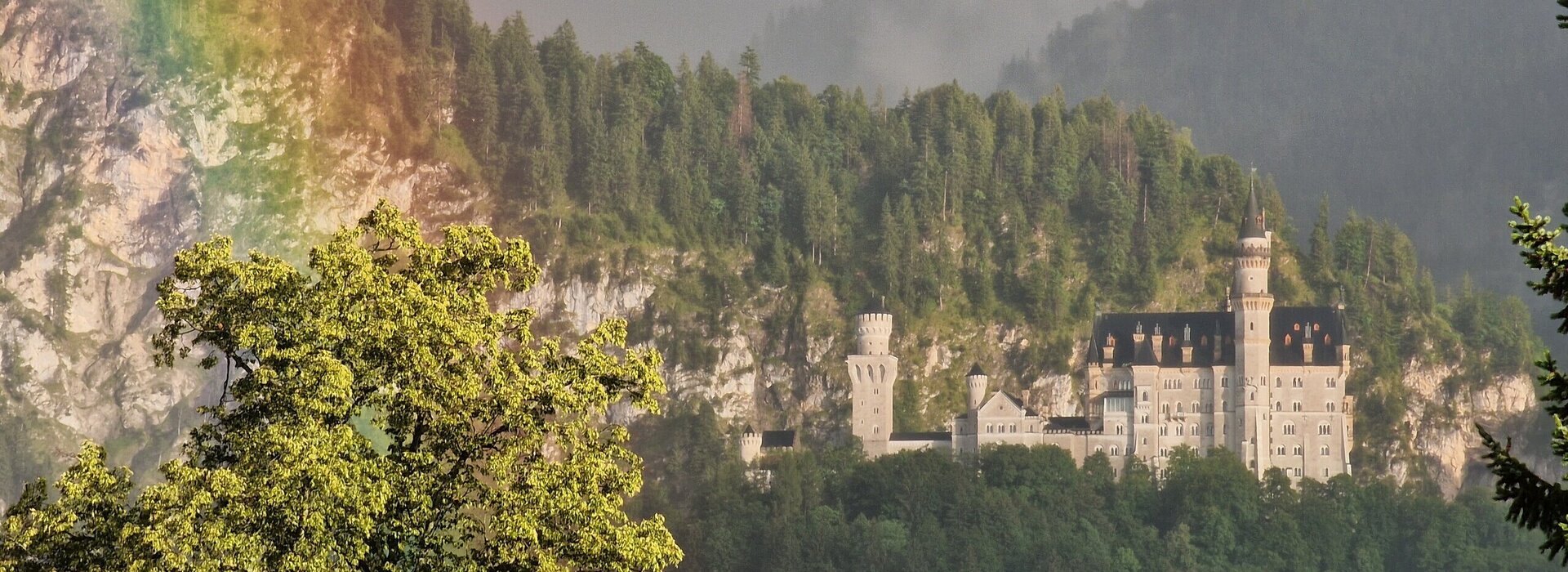 Das Foto zeigt Schloss Neuschwanstein bei Füssen im Allgäu mit einem Regenbogen.