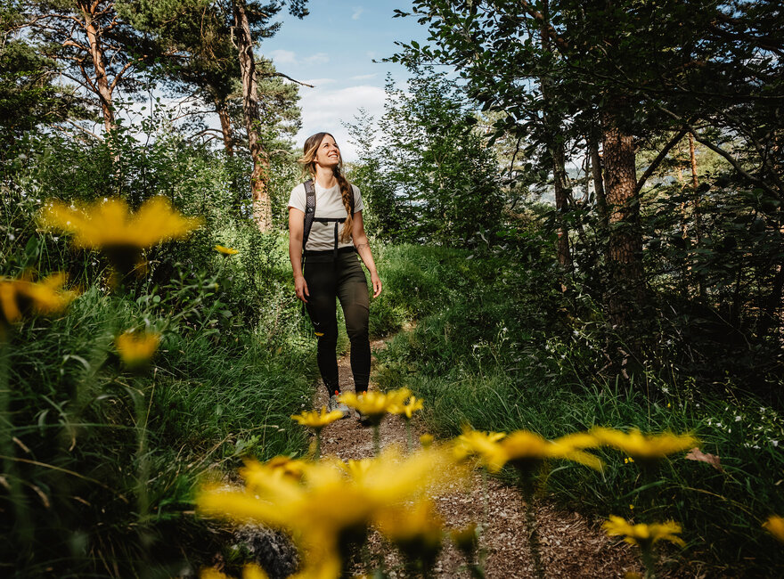 Das Bild zeigt eine Frau auf einem Wanderweg mit Blumen 