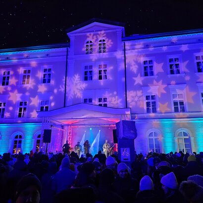 Vor einer Bühne, auf der eine Band zur Rutschparty spielt, steht ein Publikum. Das Haus hinter der Bühne ist stimmungsvoll mit Sternen angeleuchtet. 