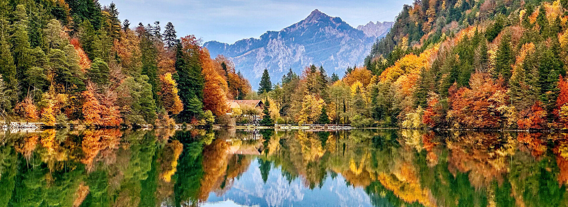 Im Fokus des Bildes liegt der Alatsee, dessen Oberfläche, glatt wie ein Spiegel, die umliegende Natur widerspiegelt. 