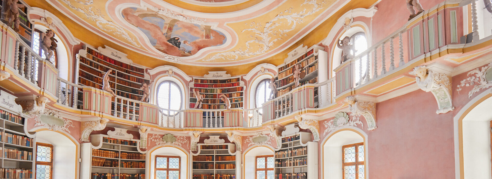 Die Bibliothek des Hohen Schlosses in Füssen mit hohen Regalen und einem beeindruckenden Rundbogen. Das Bild zeigt einen Raum voller Wissen und Geschichte.