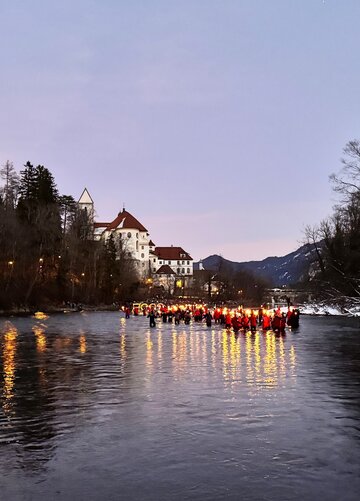 Auf dem Bild sind Schwimmer in Neoprenanzug mit Fackeln in winterlicher und abendlicher Stimmung im Lech zu sehen