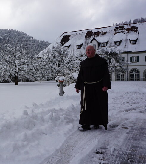 Auf dem Bild ist ein Pater im Schnee im Garten des Franziskanerklosters Füssen zu sehen