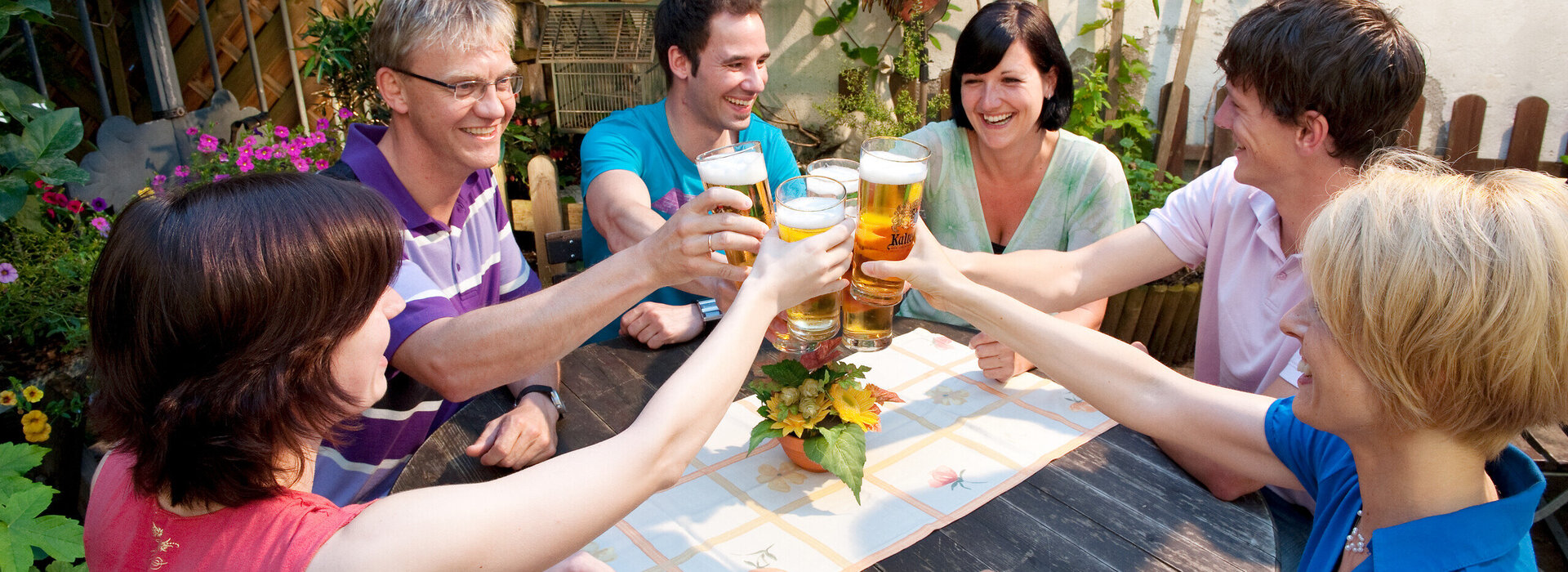 Eine fröhliche Gruppe von Freunden genießt ein Bier im Freien und feiert gemeinsam. Die entspannte Atmosphäre und die lächelnden Gesichter vermitteln ein Gefühl von Freude und Genuss.