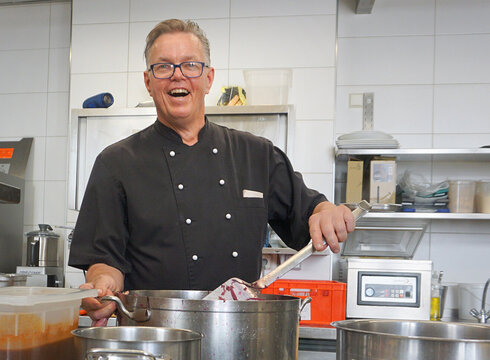 Ein Koch bereitet in der Küche des Hotel Hirsch leckere Speisen vor und lächelt.