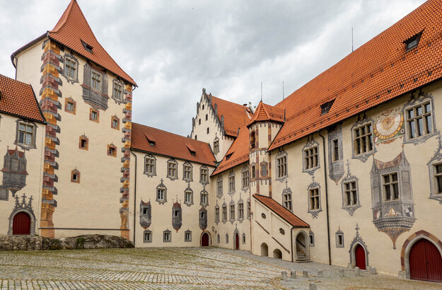 Innenhof eines mittelalterlichen Schlosses mit roten Dächern und markanten Fachwerkkonstruktionen.