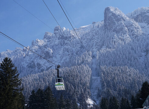 Das Foto zeigt die an einem Stahlseil hängende und talwärts oder bergwärts fahrende Kabine der Tegelbergbahn. Im Hintergrund erhebt sich der verschneite Tegelberg. Am oberen Bildrand ist die Bergstation der Bahn zu erkennen. Der Himmel ist blau. Die Sonne scheint.