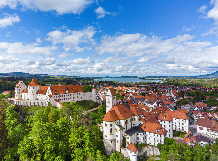 Blick auf die Altstadt von Füssen Das Bild zeigt die historische Altstadt Füssen mit dem Hohen Schloss, dem Klosterhof und dem Forggensee im Hintergrund. Der Himmel ist bewölkt.
