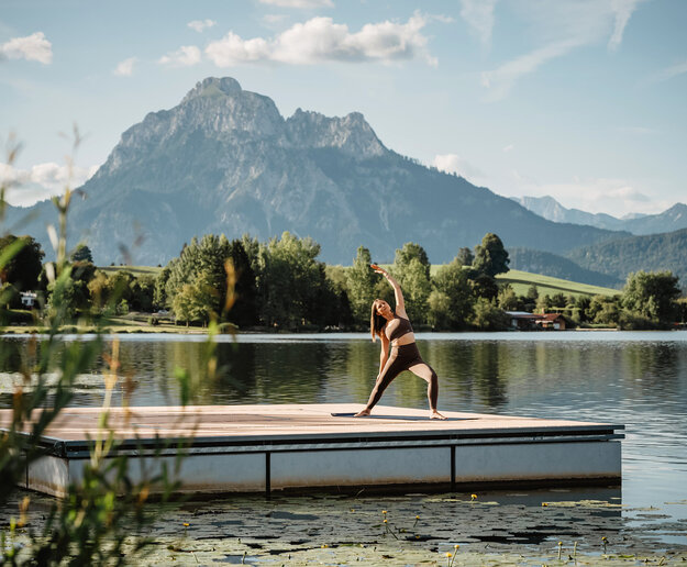 Das Bild zeigt die schwimmende Kneippinsel am Hopfensee, auf der eine Frau Yoga macht