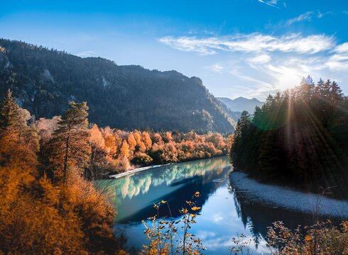Das Bild zeigt den Lech in Füssen umgeben von Wald mit herbstlich rot gefärbtem Laub.
