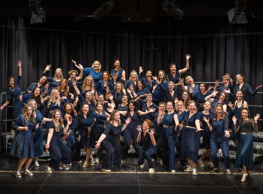 Das Bild zeigt den Chor A Capella Company und es ist eine Aufnahme von 60 Persoonen die in die Kamera jubeln.