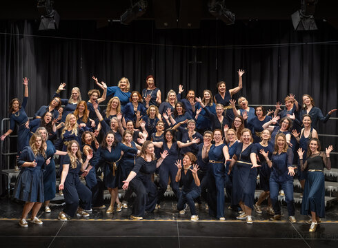 Das Bild zeigt den Chor A Capella Company und es ist eine Aufnahme von 60 Persoonen die in die Kamera jubeln.